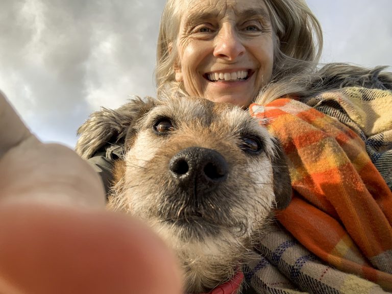 A selfie shot of a mature woman wearing warm clothing with her senior patterdale terrier while standing outdoors in Northumberland. They are both looking at the camera and the woman is smiling.